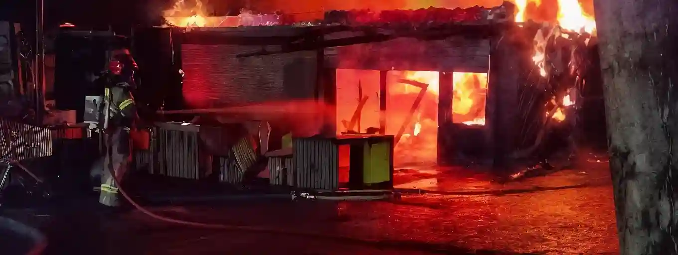 Nachtelijke brand bij ParkNest in het Flevopark met uitslaande rode en oranje vlammen en een brandweerman in actie.